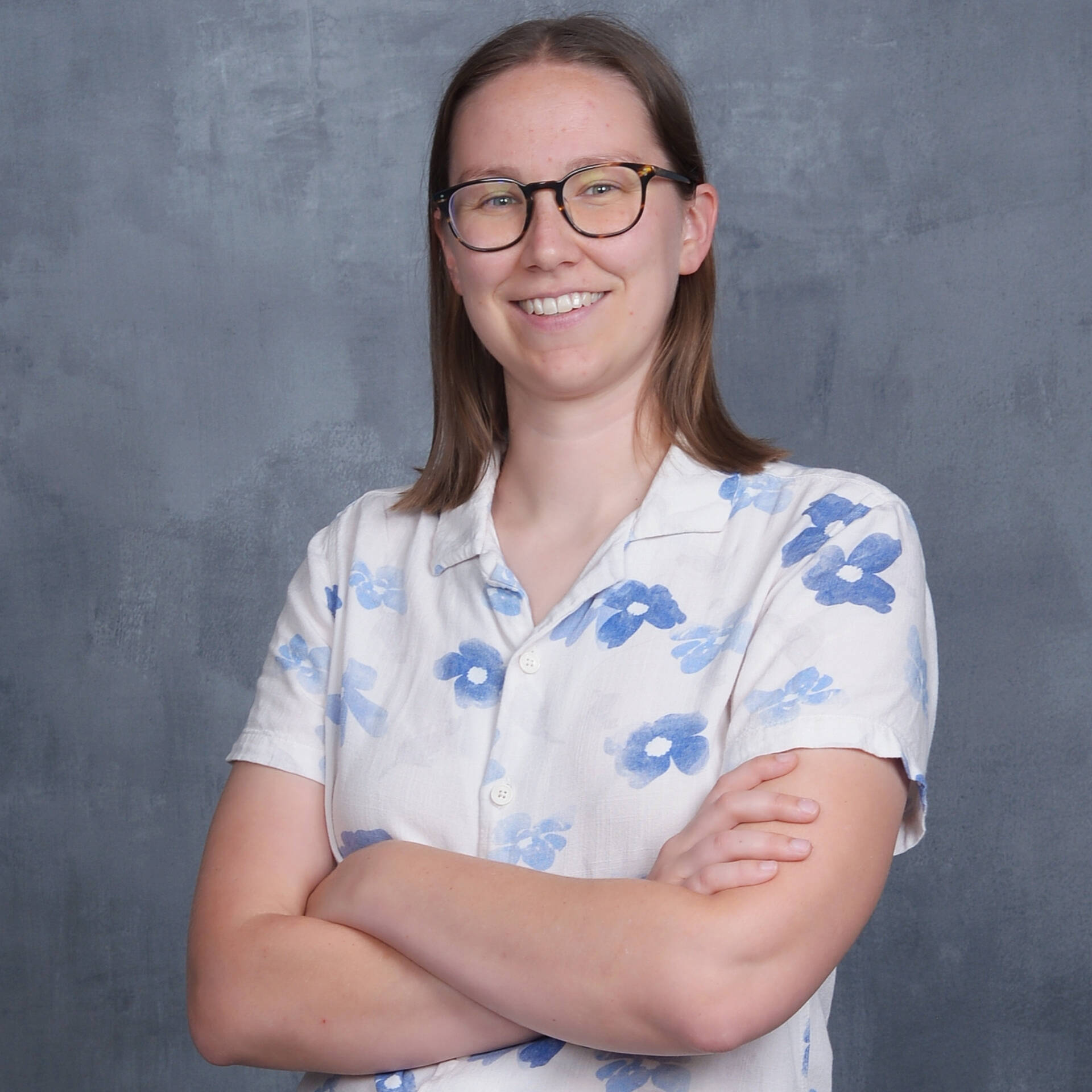 Joey, with dark roundish glasses, shoulder length brown hair, and a white collared shirt with pale blue flowers
